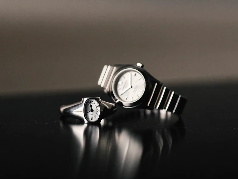 Illustration: Silberring und Armbanduhr auf glänzend schwarzem Acryl mit weichen Reflexionen